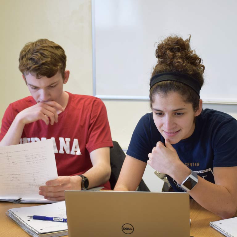 Two students use a laptop to work on a project together. 